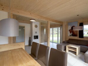 A modern interior with a wooden ceiling, a dining area with a table and chairs, a living room with a sofa and a coffee table, and a large window with a view of the outdoors. - One-bedroom Cabin (Sankt Georgen am Kreischberg)