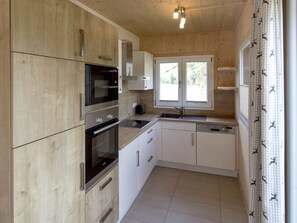 A modern kitchen with wooden cabinets, stainless steel appliances, and a window providing natural light. - One-bedroom Cabin (Sankt Georgen am Kreischberg)