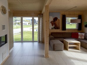 A spacious living room with a large window, a sofa, a coffee table, and a painting of a cow. - One-bedroom Cabin (Sankt Georgen am Kreischberg)