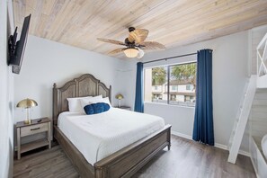 Une chambre avec un plafond en bois, un lit avec une literie blanche, une table de chevet avec une lampe et une fenêtre avec des rideaux.