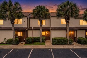 A multi-story building with a row of windows, a parking lot in front, and palm trees. - Coastal Retreat at Beachwalk, Steps from the Gulf (Panama City Beach)