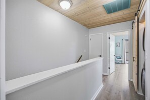 A hallway with a white wall, a wooden ceiling, and a white door at the end. - Coastal Retreat at Beachwalk, Steps from the Gulf (Panama City Beach)