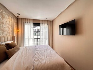 Habitació d'hotel amb un llit, cortines, televisió penjada i una làmpada fixada a la paret.