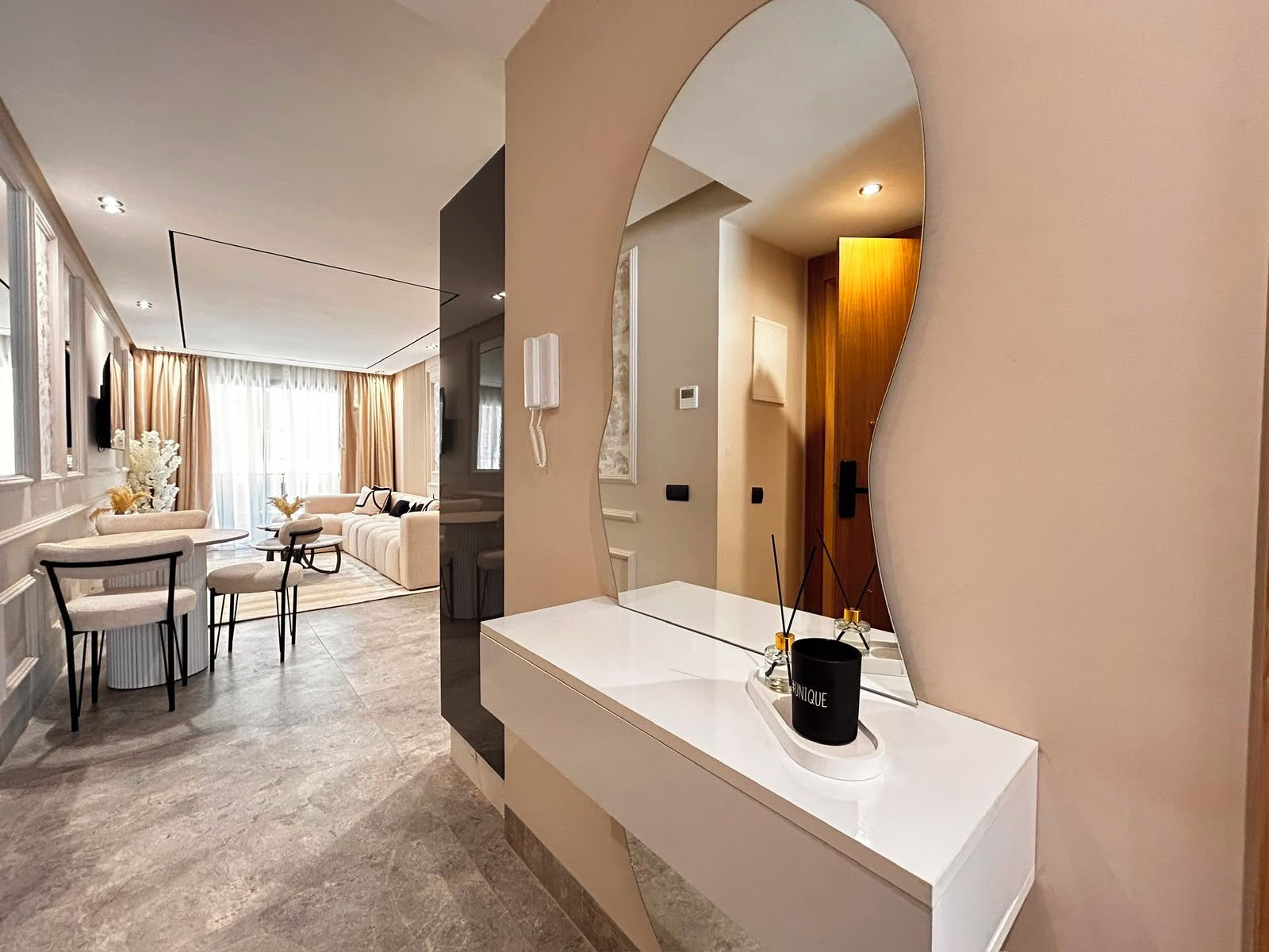 Une chambre d’hôtel moderne dotée d’un grand miroir, d’une coiffeuse blanche et d’un coin salon avec un canapé et des fauteuils.