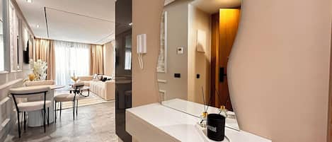 A modern hotel room with a large mirror, a white vanity, and a seating area with a sofa and chairs.