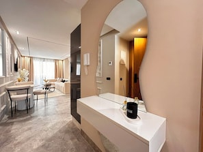 Habitació d'hotel moderna amb un mirall gran, una tocador blanc i una zona de seients amb un sofà i cadires.
