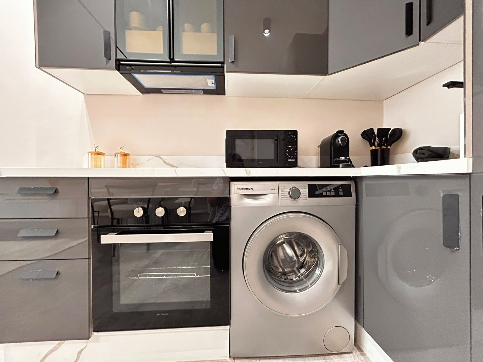 Une cuisine compacte équipée d’un four, d’un micro-ondes et d’un lave-linge intégrés.