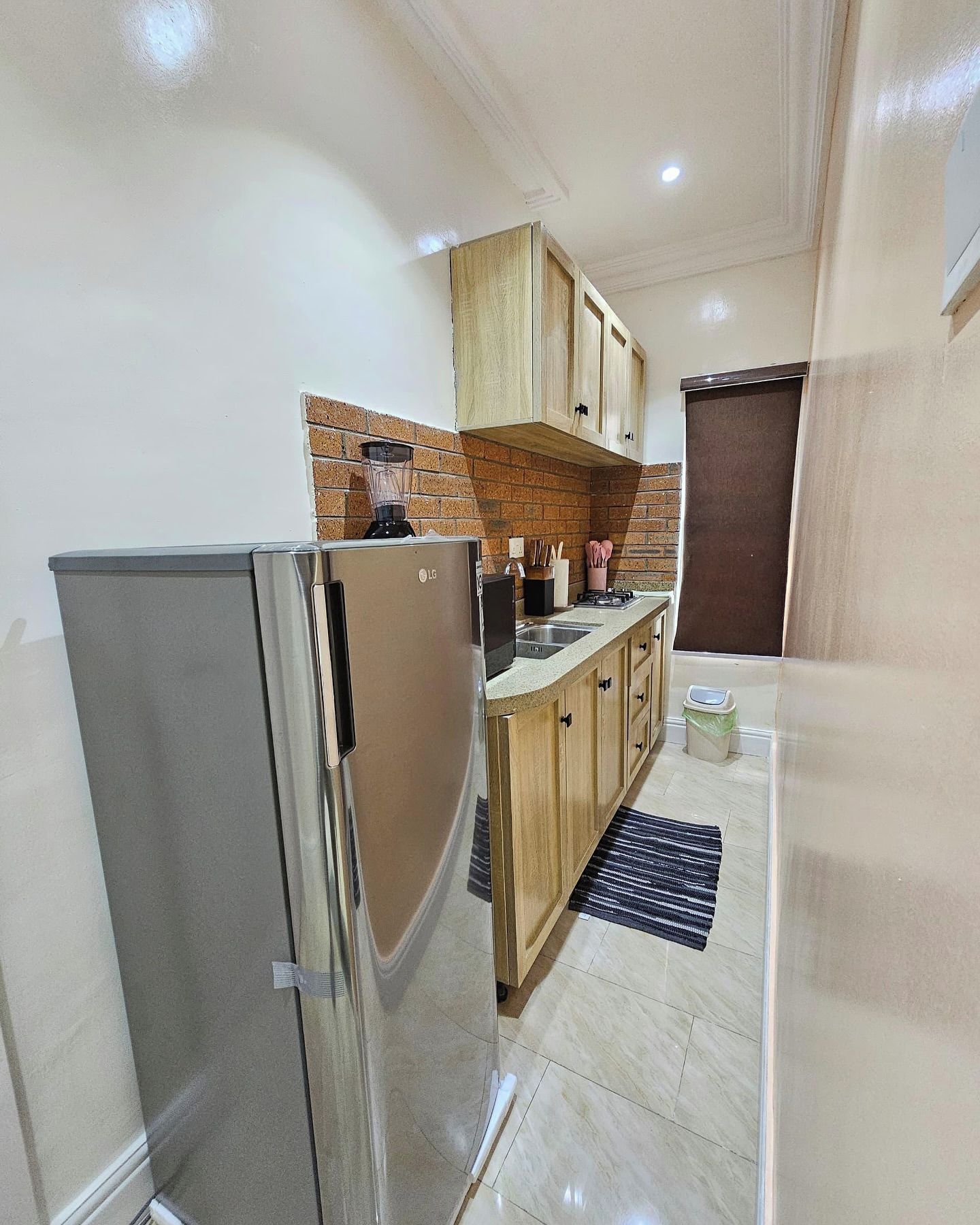 A compact kitchen with a refrigerator, wooden cabinets, a brick backsplash, and a small countertop.