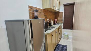 A compact kitchen with a refrigerator, wooden cabinets, a brick backsplash, and a small countertop.