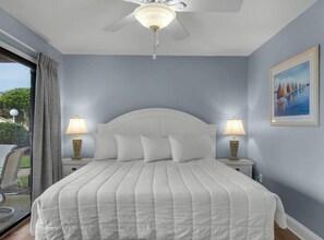 A bedroom with a bed, two bedside lamps, a ceiling fan, and a painting on the wall. - Blue Surf 4 (Miramar Beach)