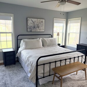 Une chambre à coucher avec un lit, des tables de chevet, un banc et un ventilateur de plafond.
