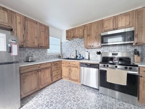 A kitchen with wooden cabinets, stainless steel appliances, and patterned tile flooring. - Beautiful, 2-bedroom house with AC, fast WiFi, quiet street, close to downtown. (Corpus Christi)