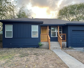 A single-story house with a front porch, a garage, and a small front yard. - Beautiful, 2-bedroom house with AC, fast WiFi, quiet street, close to downtown. (Corpus Christi)
