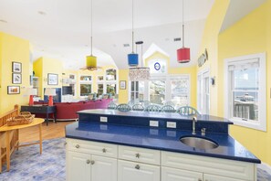 A bright kitchen with a blue countertop, white cabinets, and a large window. - Soundfront w/ Hot Tub, Game Room & Resort Perks! (Corolla)