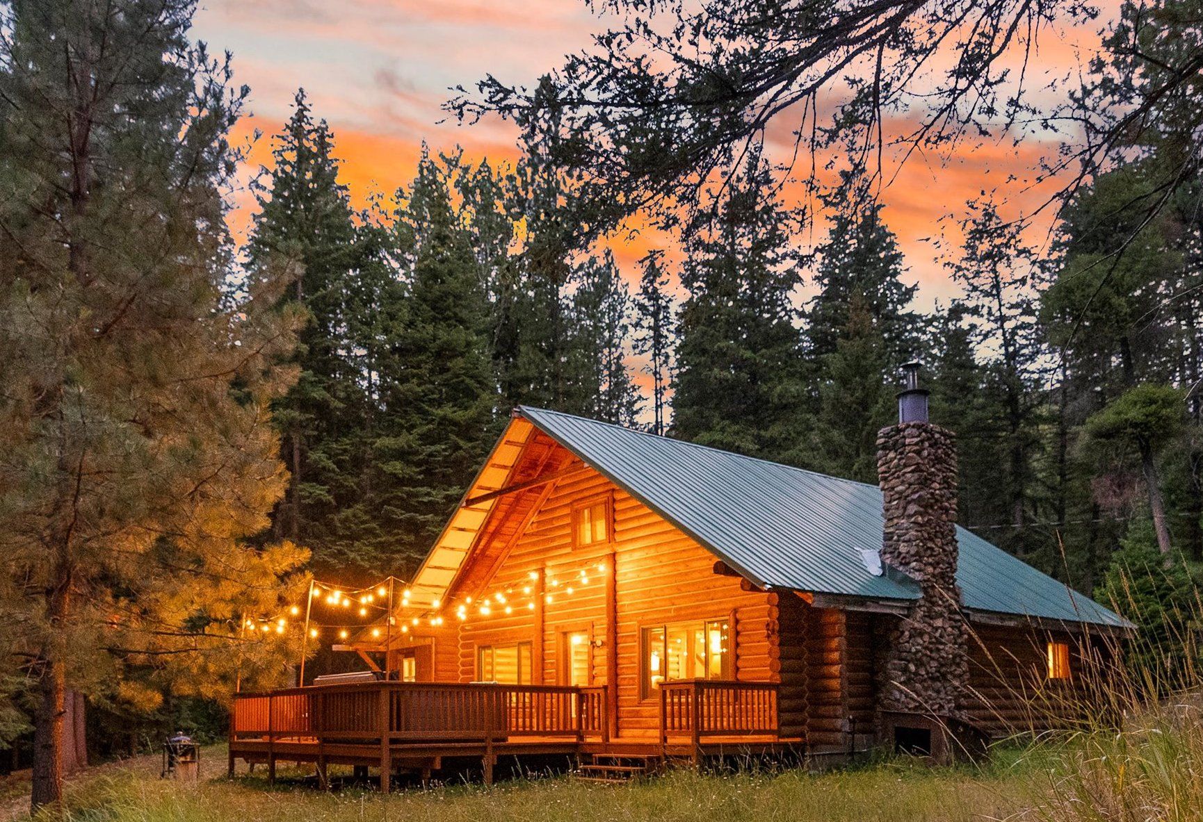 A log cabin with a stone chimney, wooden deck, and string lights.