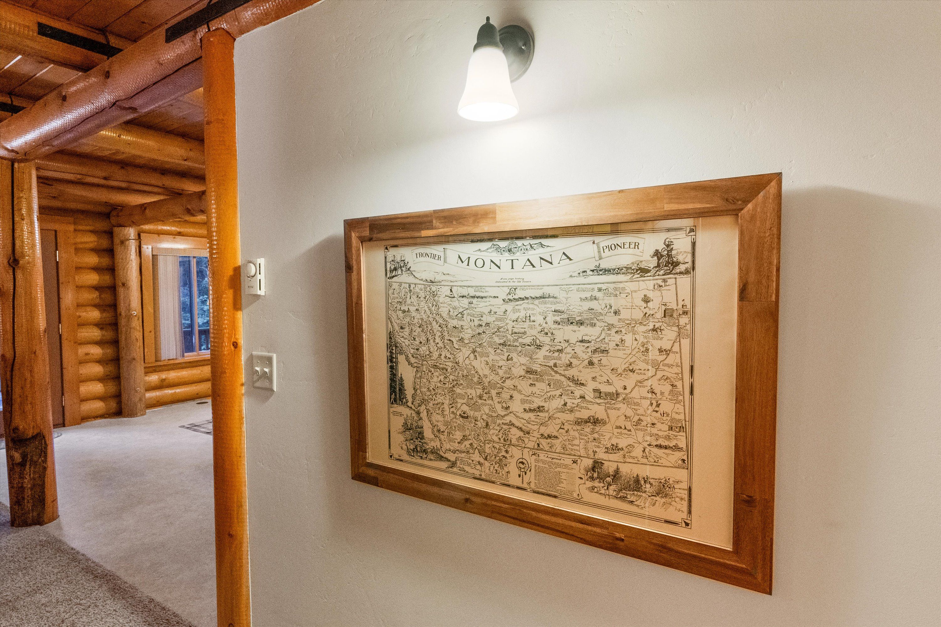 Un mapa histórico de Montana enmarcado cuelga en una pared de una habitación al estilo de cabaña de troncos, con vigas de madera y un accesorio de iluminación arriba.