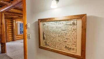 Un mapa histórico de Montana enmarcado cuelga en una pared de una habitación al estilo de cabaña de troncos, con vigas de madera y un accesorio de iluminación arriba.
