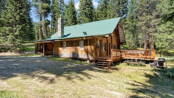 A log cabin with a green metal roof, wooden deck, and a chimney.
