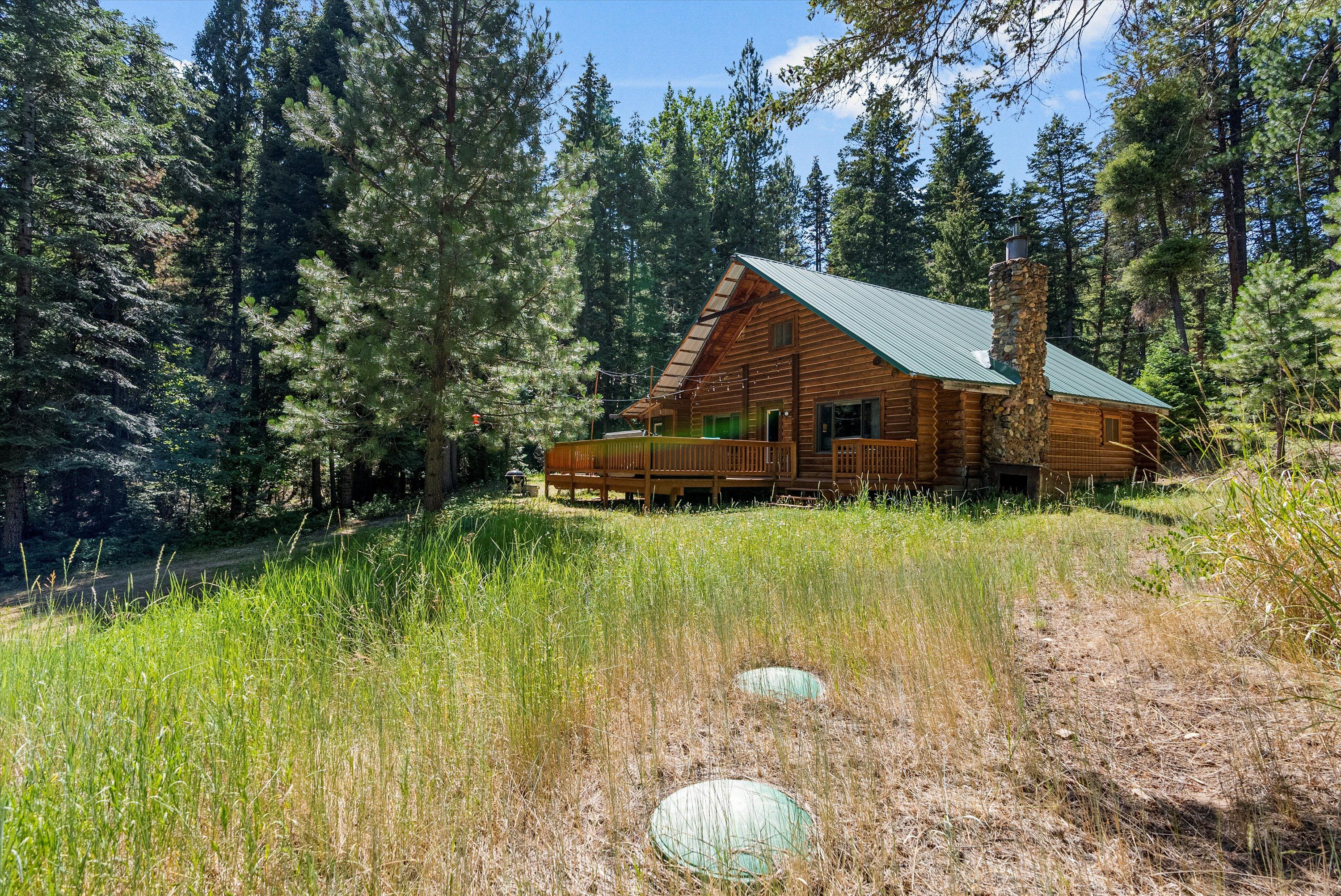 Une cabane en rondins dotée d’un porche, entourée d’une forêt dense.