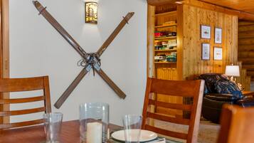 A wooden interior with a dining table set for two, a candle centerpiece, and a wall-mounted crossbow.