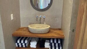 Ein Badezimmer mit einem runden Waschbecken, einem Spiegel darüber und einem Ablagefach mit gefalteten Handtüchern.