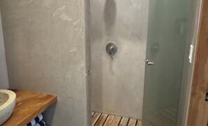 A bathroom with a wooden shelf, a stone basin, and a glass shower enclosure. - Modern Nosara Casita - 5 Min Walk to Beach (Nosara)