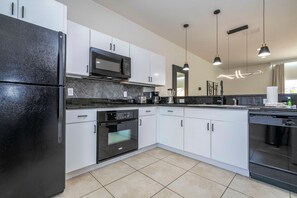A modern kitchen with white cabinets, a black refrigerator, a microwave, and a dishwasher. - 3BR Themed Rooms Near Disney Private hot tub (Kissimmee)