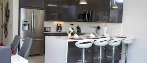 A modern kitchen with dark cabinetry, stainless steel appliances, and a central island with bar stools.