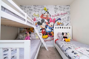 Ein Kinderzimmer mit Etagenbetten, einer Wandmalerei von Disney-Figuren und Mickey Maus Stofftieren.