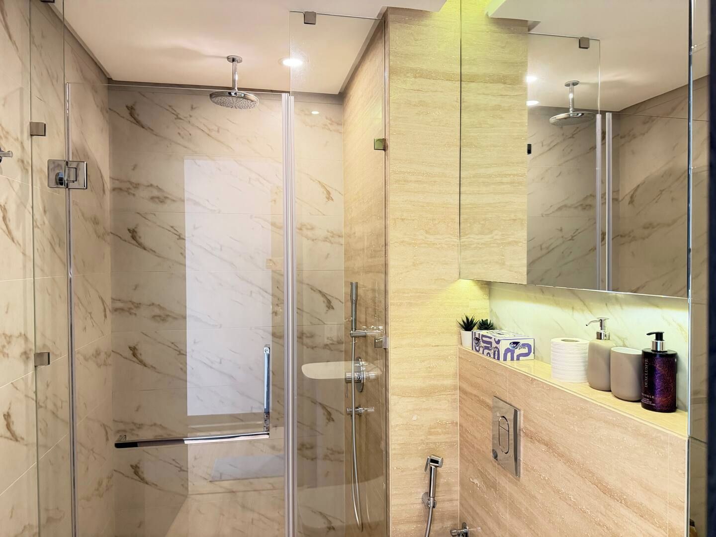 Une salle de bain moderne avec une douche à parois de verre, des murs en marbre et un meuble-lavabo avec des articles de toilette.