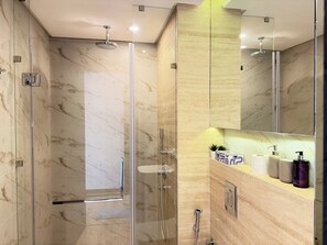 A modern bathroom with a glass-enclosed shower, marble walls, and a vanity with toiletries. - Stunning Four Seasons Views by Flouri FBB913O (Manama)