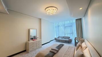 A modern bedroom with a large bed, a dresser, a sofa, and a large window with curtains.