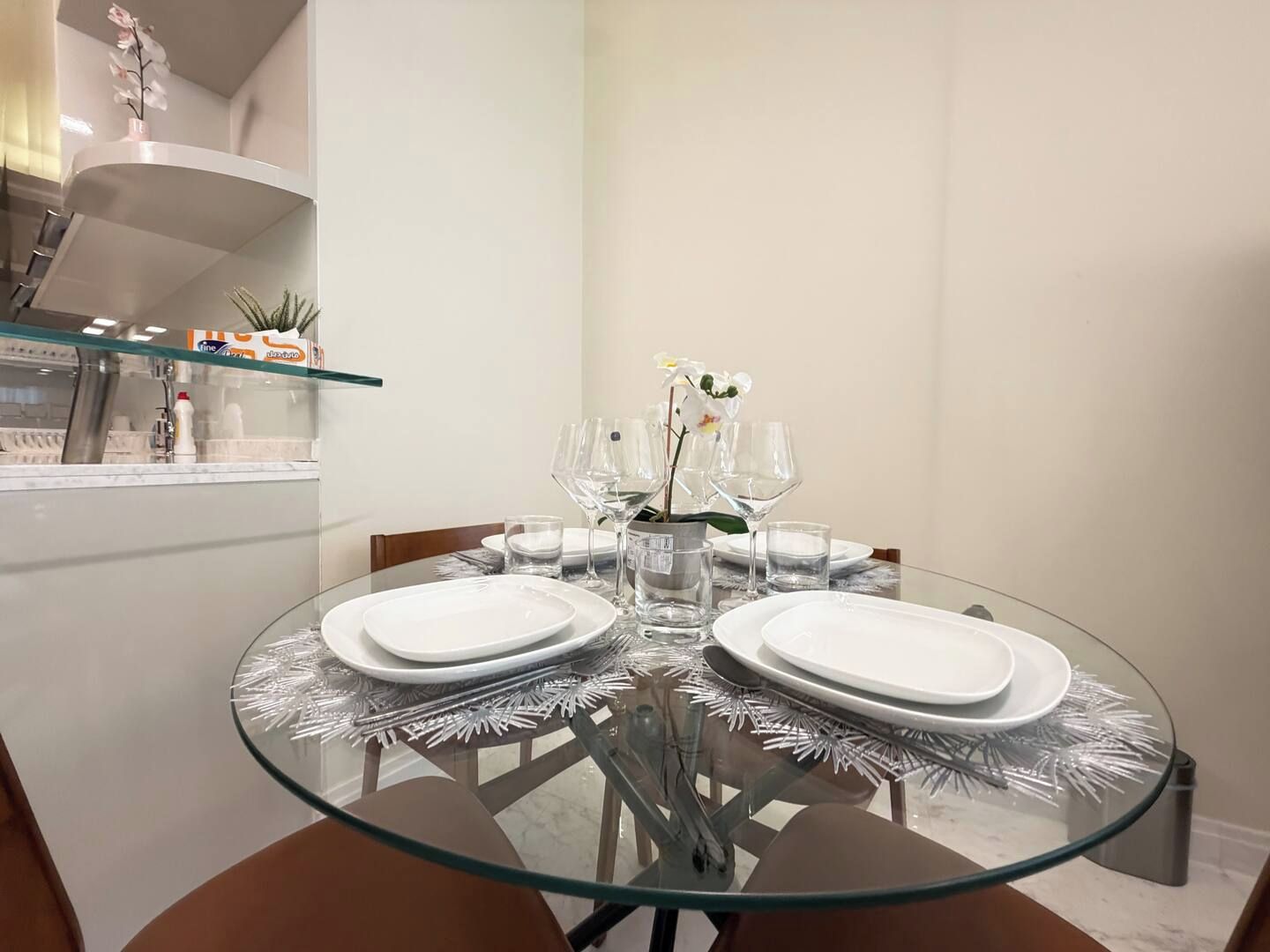 Un'area pranzo con tavolo in vetro circondato da sedie, piatti bianchi e bicchieri trasparenti.