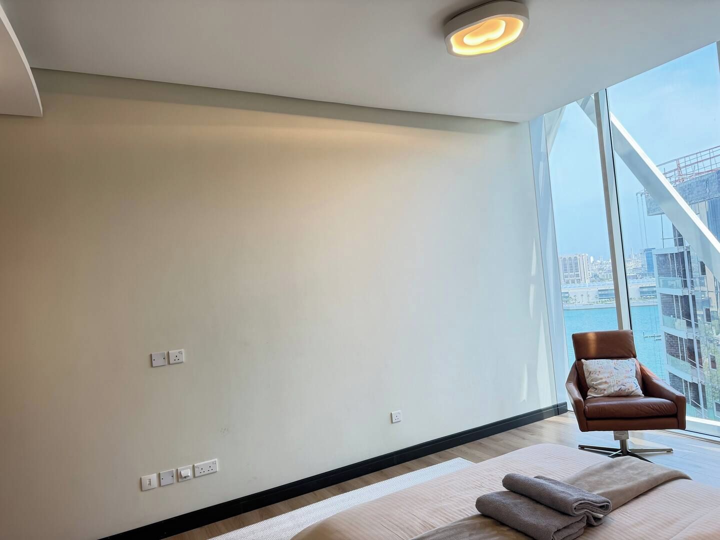 Ein modernes Hotelzimmer mit großem Fenster, einem Bett, einem braunen Ledersessel und Blick auf die Stadt.