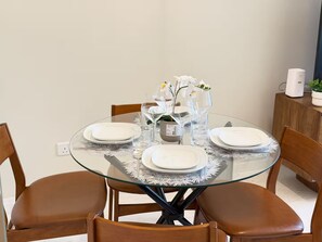 A round glass dining table with white plates, clear glassware, and a vase with white flowers. - Stunning Four Seasons Views by Flouri FBB913O (Manama)