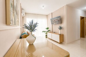 A modern living room with a wooden coffee table, a white vase with blue flowers, a flat-screen TV mounted on the wall, and a wooden console table with a plant. - Group Vacation • Ocean View • Swimming Pool (Cartagena)