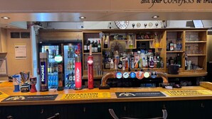 Eine Bar mit einer Auswahl an Spirituosenflaschen und einem Schild mit der Aufschrift 'The Akston The Original Mechanical Craft Brewer'.