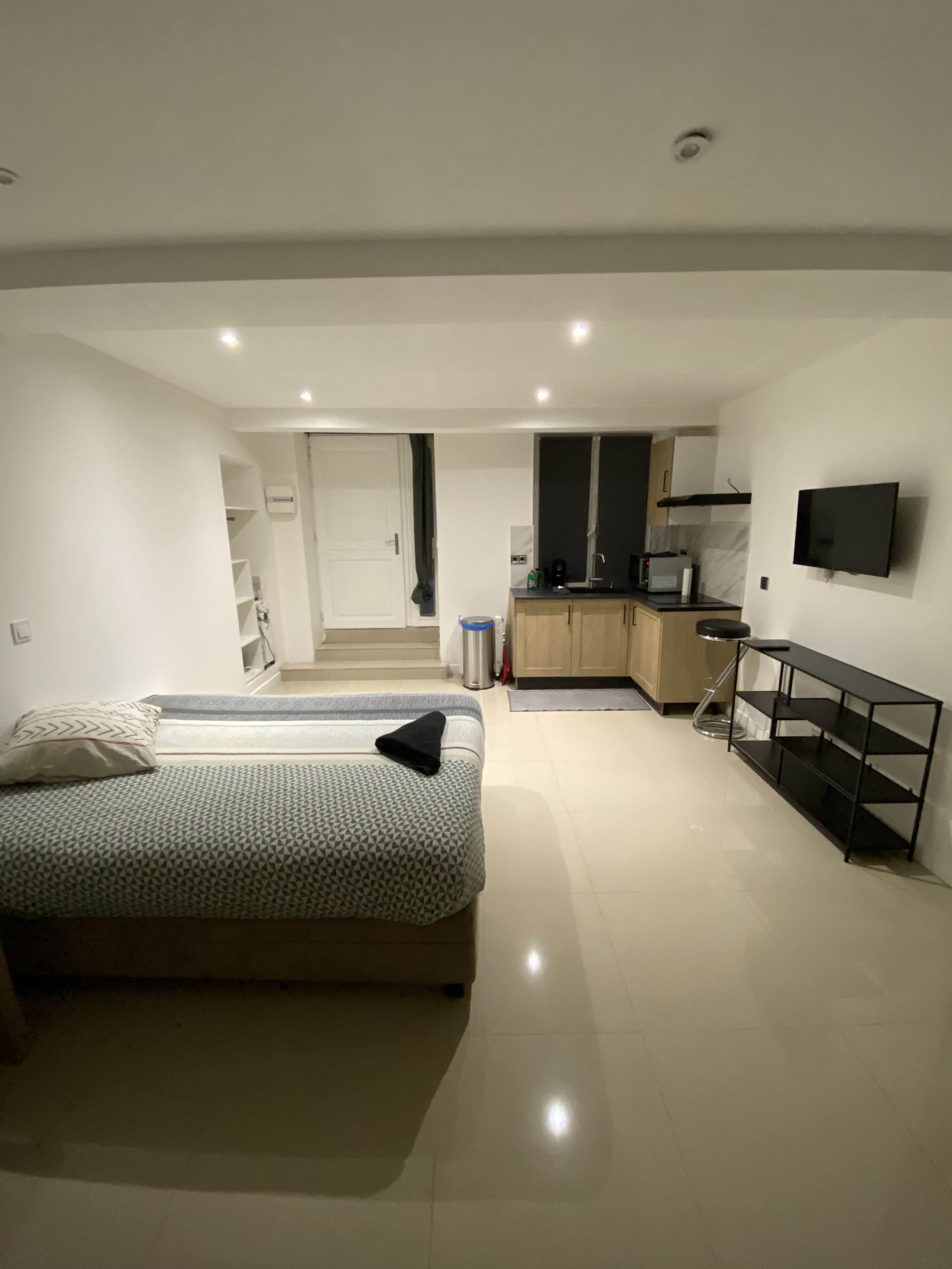Een moderne slaapkamer met een bed, een televisie en een kitchenette op de achtergrond.