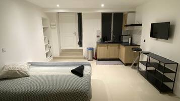Een moderne slaapkamer met een bed, een televisie en een kitchenette op de achtergrond.