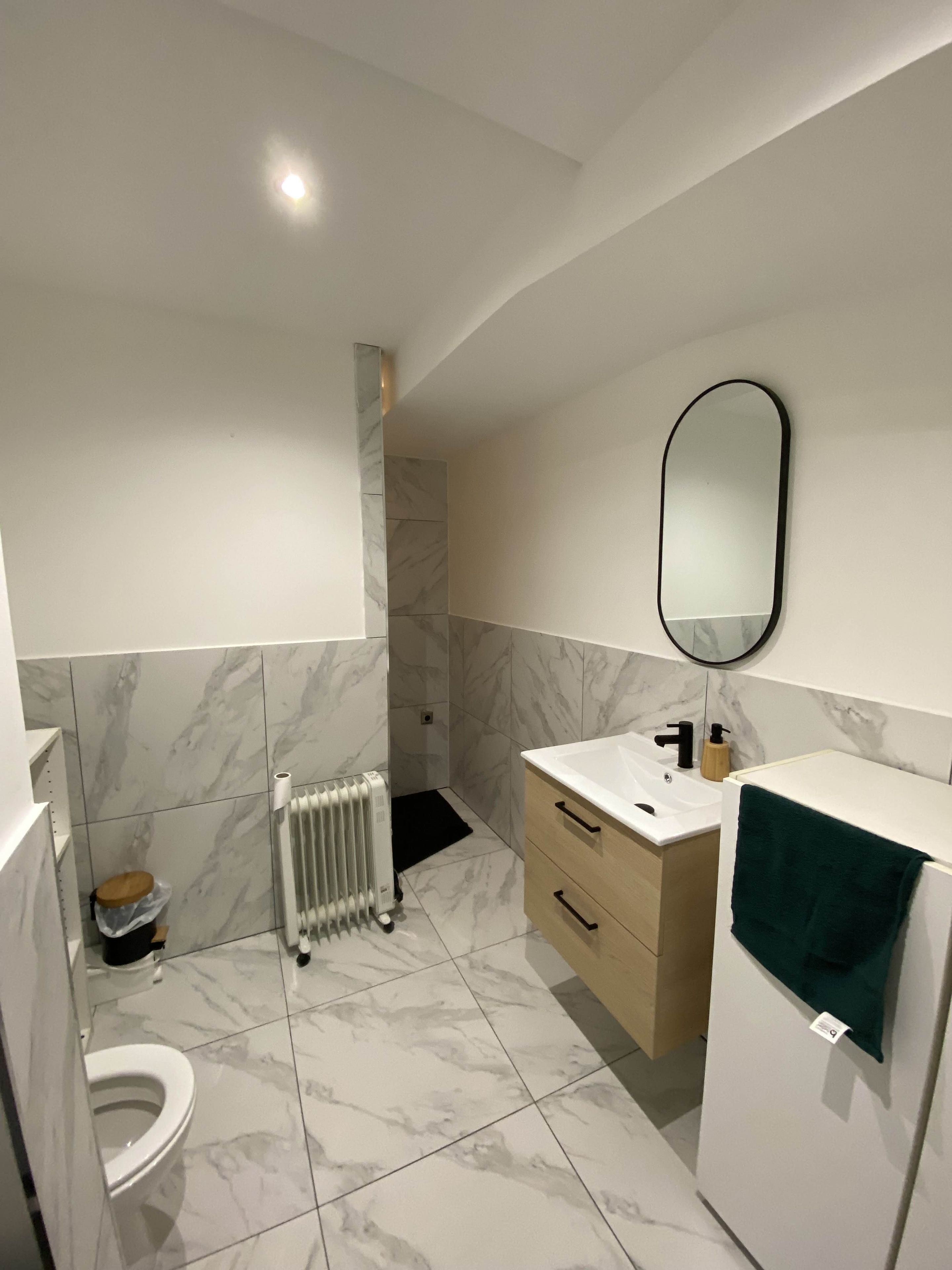 Een moderne badkamer met toilet, wastafel, spiegel en radiator.