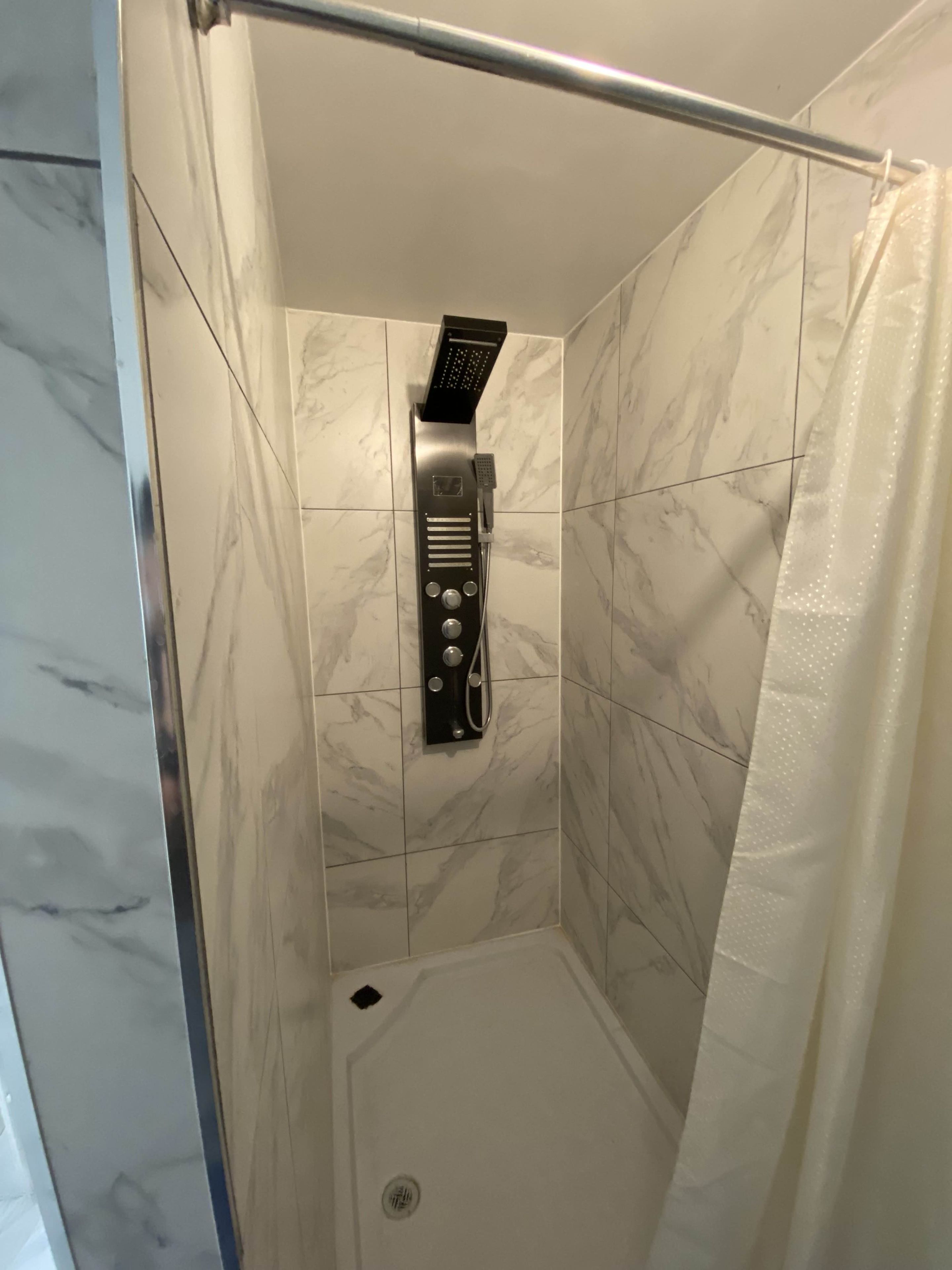 Een douche met een handdouche en bedieningspaneel, in een ruimte met marmeren tegels.