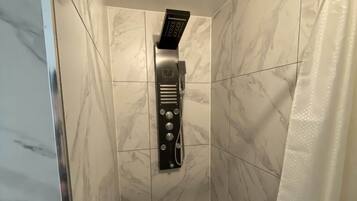 Een douche met een handdouche en bedieningspaneel, in een ruimte met marmeren tegels.