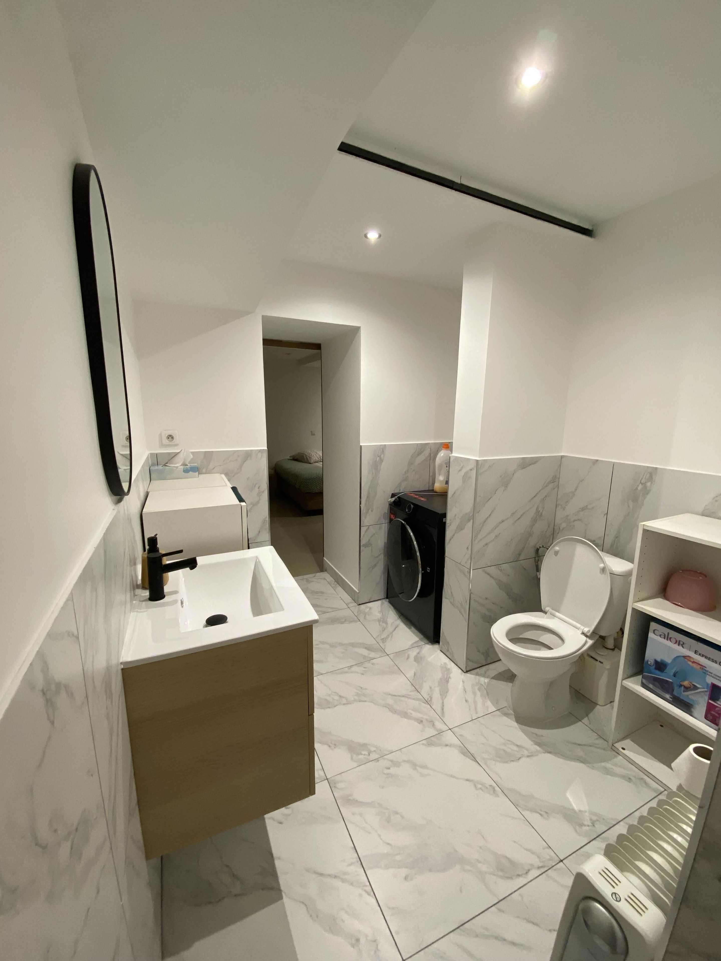 Een moderne badkamer met een wastafel, toilet en wasmachine, met marmeren vloeren en een houten kast.