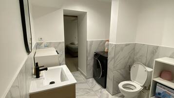 Een moderne badkamer met een wastafel, toilet en wasmachine, met marmeren vloeren en een houten kast.