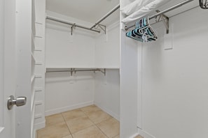 Ein begehbarer Kleiderschrank mit zwei Metallstangen zur Kleidaufbewahrung, einem gefliesten Boden und einer weißen Tür.