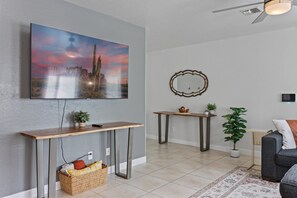 En stue med et ophængt fjernsyn, et konsolbord, et sofabord, et spejl, en sofa og en tæppe med et mønster.