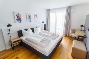 A hotel room with two beds, a desk, and a chair. There are artworks on the wall and a window with curtains. - Luxury Historic Apartment in Central Berlin 3 Bedrooms (Berlin)