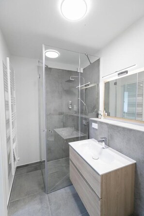 Ein modernes Badezimmer mit einer gläsernen Duschkabine, einem Holzkosmetikschrank und einem Spiegel über dem Waschbecken.