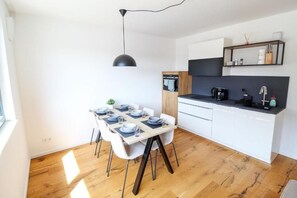 Eine moderne Küche mit weißen Schränken, einer schwarzen Arbeitsplatte und einem Essbereich mit einem Holztisch für vier Personen.