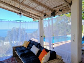 Ein überdachter Außenbereich mit Blick auf einen Swimmingpool und das Meer.